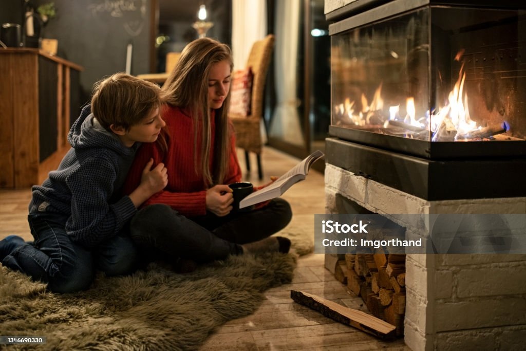 Two kids reading by the fire